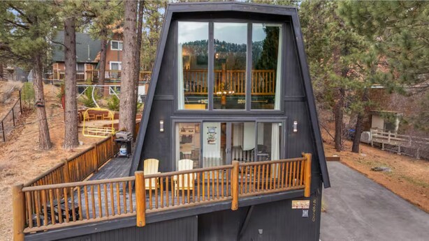 Eine moderne Hütte mit Terrasse, großen Fenstern und Blick auf den umliegenden Wald.