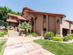 A multi-story building with a 'B' sign, a landscaped front yard, and a clear sky. - Sports Village Condo | Pools, Courts & Trails (St. George)