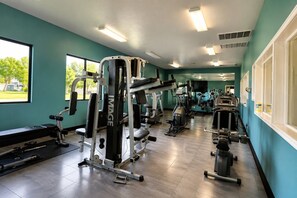 A gym with various exercise equipment, large windows, and a view of greenery outside. - Sports Village Condo | Pools, Courts & Trails (St. George)