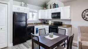 A compact kitchen with white cabinets, a black refrigerator, a microwave, and a dining area with a table and chairs. - Sports Village Condo | Pools, Courts & Trails (St. George)
