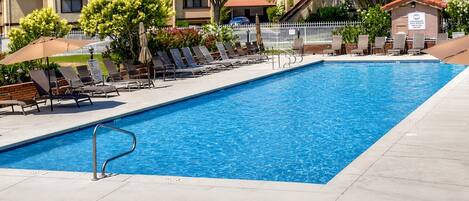 A rectangular swimming pool with a metal ladder, surrounded by lounge chairs and umbrellas.