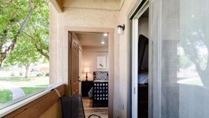 A balcony with a chair, a door leading to a room, and a view of a garden. - Sports Village Condo | Pools, Courts & Trails (St. George)