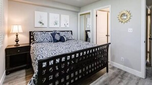 A bedroom with a bed, nightstand, wall art, and a door. - Sports Village Condo | Pools, Courts & Trails (St. George)