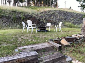 A patio with white chairs and a fire pit in a natural setting. - Elk Ridge Vacation Home, 3 bedrooms, 1 bath, downtown Hill City (Hill City)