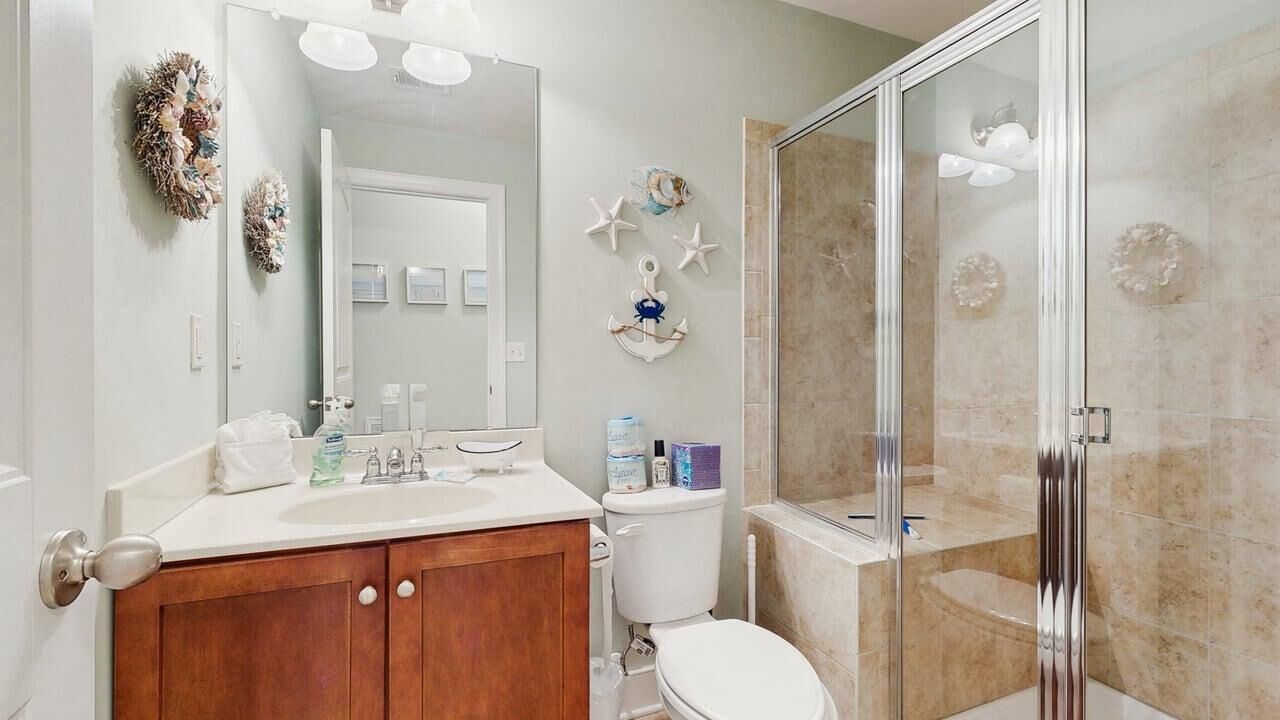 A bathroom with a wooden vanity, a toilet, a shower with glass doors, and wall decorations including starfish and an anchor.