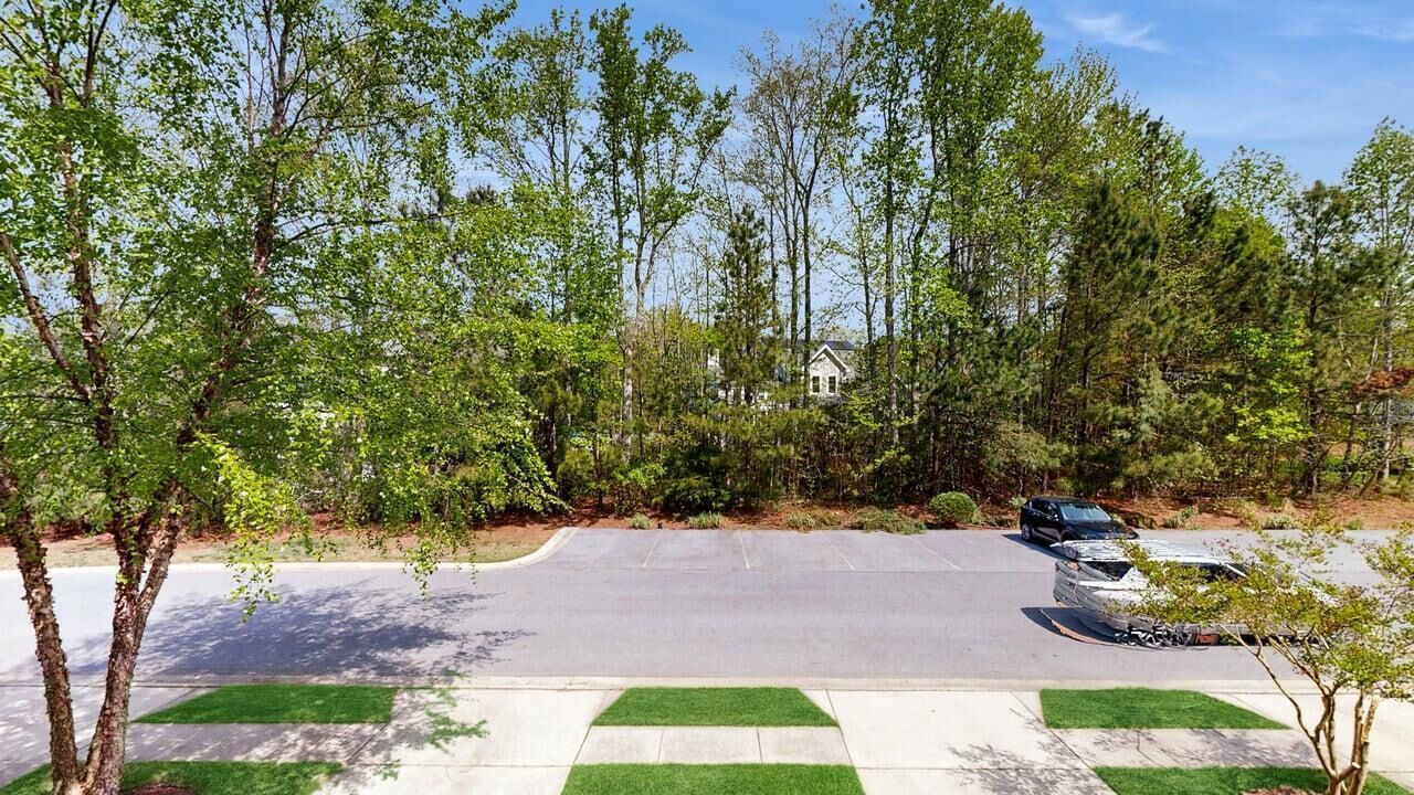 Un parking avec un bâtiment en arrière-plan, entouré d’arbres et de verdure.