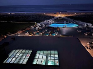 Ein Poolbereich auf dem Dach mit Blick auf den Ozean, Sitzgelegenheiten im Freien und einer überdachten Brückenkonstruktion.