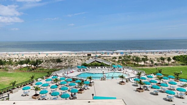 Resort com área de piscina, vista para a praia e mobiliário de exterior com guarda-sóis.