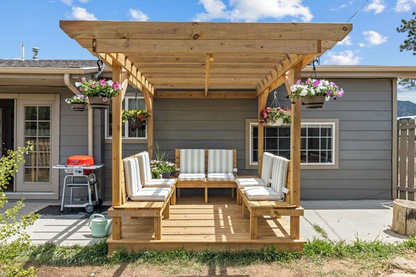 Une pergola en bois avec un banc et des jardinières suspendues devant une maison.