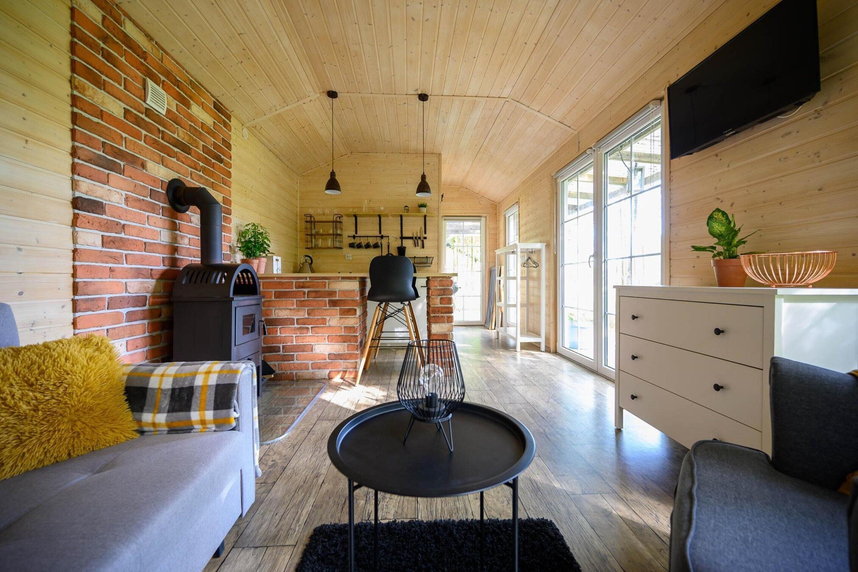 Un interior acogedor con pared de ladrillo, techo de madera, un sofá, una mesa de comedor y una zona de cocina.
