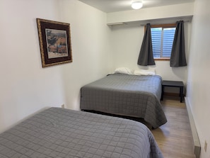 Ein Schlafzimmer mit zwei Betten, einem kleinen Tisch, einem Fenster mit VorhÀngen und einem gerahmten Bild an der Wand.