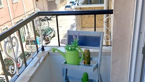 Un balcone con un piccolo tavolo, un annaffiatoio verde, un cactus e una pianta in vaso.