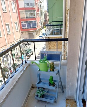 Ein Balkon mit einem kleinen Tisch, einem grünen Wasserkrug, einem Kaktus und einer Topfpflanze.