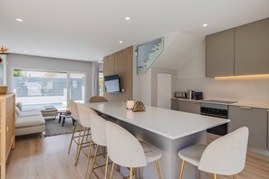 Cozinha moderna com ilha central, banquetas, TV de tela plana e escada.