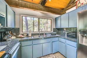 A kitchen with blue cabinets, a stainless steel refrigerator, a window with a view of trees, and a granite countertop. - Sedona Wellness Retreat Near Trails & Downtown (Sedona)