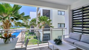 A balcony with a pool view, a sofa, a table, and potted plants.
