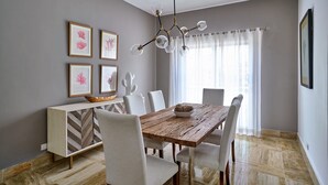 A dining area with a wooden table, white chairs, a chandelier, and framed artwork on the wall.