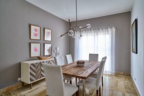 Ein Essbereich mit Holztisch, weißen Stühlen, einer Kandelaber und gerahmten Kunstwerken an der Wand.
