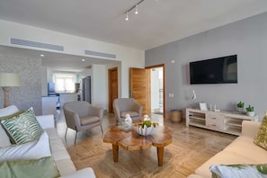Ein modernes Wohnzimmer mit einer Couch, Sesseln, einem Couchtisch und einem Fernseher.
