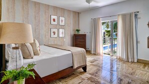 A bedroom with a bed, a ceiling fan, a nightstand with a lamp, a dresser, and a window with curtains.