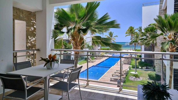 A balcony with a pool view, a dining area with chairs and a table, and a potted plant.