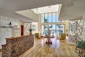 A lobby with a reception desk, seating area, and large windows offering a view of the outdoors. - Apartment - Ground Floor (Punta Cana)