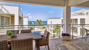 A balcony with a view of the ocean, a dining table with chairs, and a wicker sofa. - Oceanfront Penthouse w/Rooftop, Pool, Punta Cana (Punta Cana)
