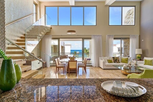 A spacious living area with a dining set, a staircase, and large windows offering a view of the sea. - Luxury Oceanfront Penthouse in Punta Cana (Punta Cana)