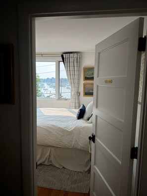 Ein Schlafzimmer mit Bett, einem Fenster mit Blick auf Boote und einer Tür mit Namensschild.