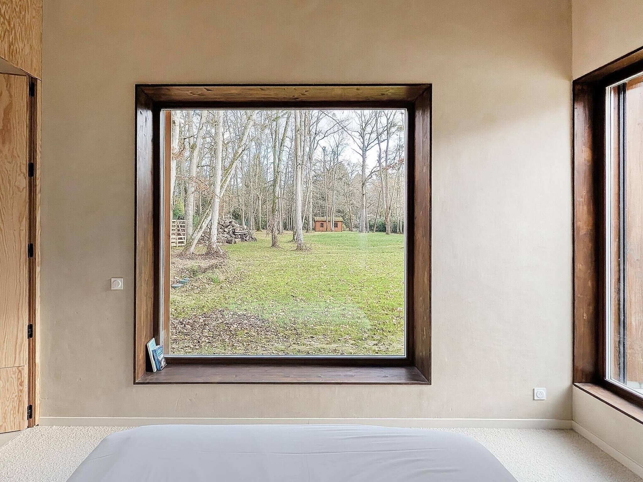 Een kamer met een groot raam, een bed en uitzicht op een grasveld met bomen.