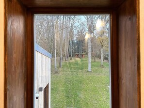 Una puerta de madera que da a un patio cubierto de césped, con árboles y un edificio pequeño al fondo.