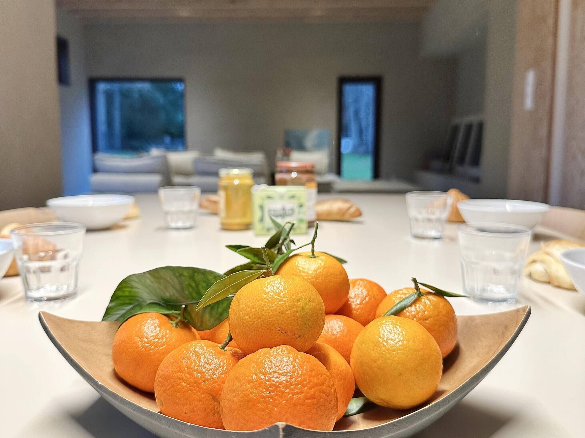 Een eettafel met een schaal mandarijnen, glazen en een paar gebakjes.