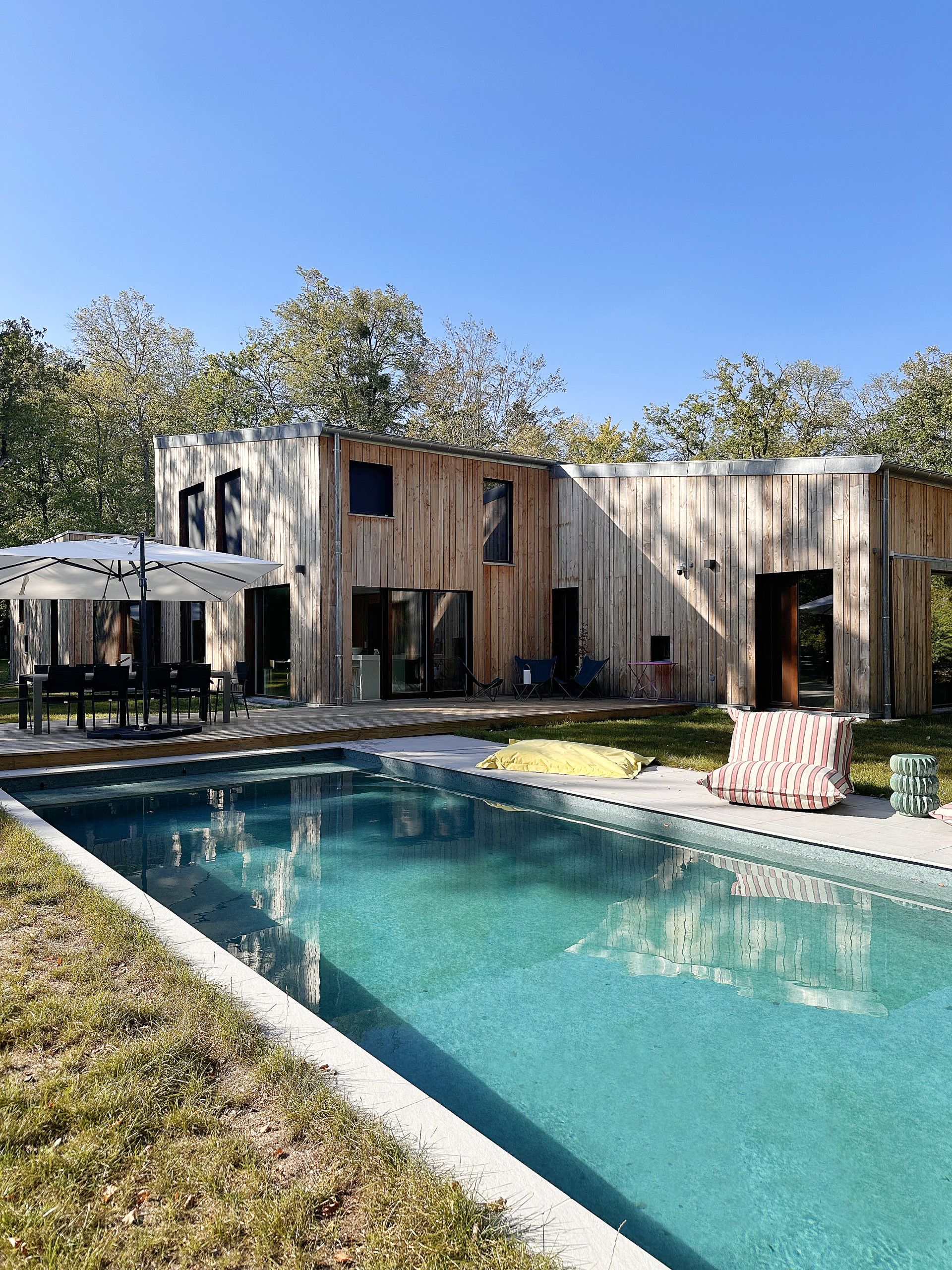 A modern outdoor pool area with a wooden deck, lounge chairs, and a covered seating area.