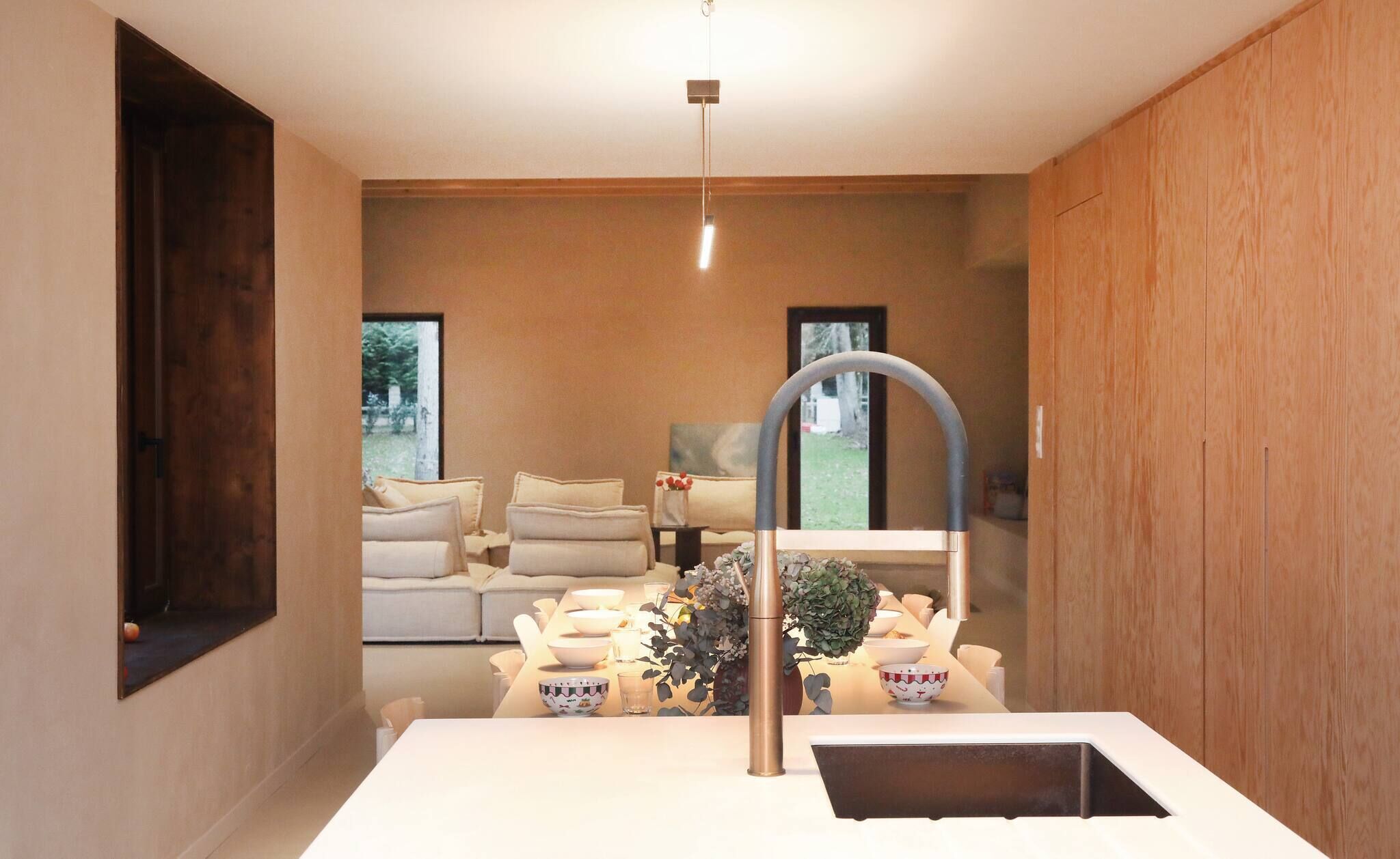 Eine moderne Küche mit einer zentralen Kochinsel, einer Hängelampe und Blick auf einen Wohnbereich mit Sofa und Gemälde.