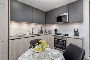 Een moderne keuken met grijze kastjes, een magnetron, een spoelbak en een eethoek met een tafel gedekt voor twee personen.