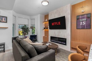 Ein modernes Wohnzimmer mit einer Couch, einem Couchtisch, einem Flachbildfernseher, einem Kamin und einem Basketballtrikot an der Wand.