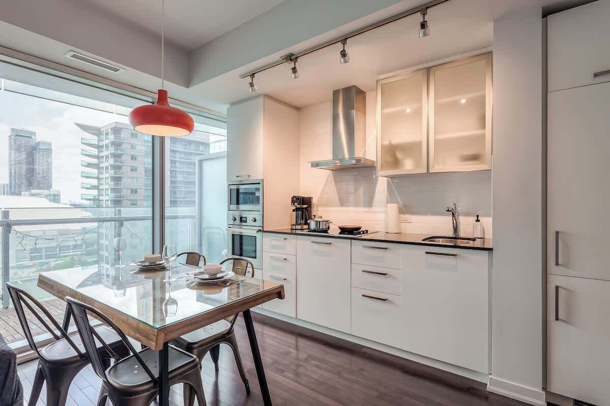 Een moderne keuken met een glazen eettafel, witte kastjes en uitzicht op de stad.