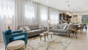 A modern living room with a sofa, chairs, and a dining area with a table and chairs. - Chic Orlando Escape Game Room Theme Beds Pool (Clermont)