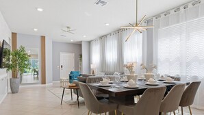 A modern dining area with a large table set for six, surrounded by grey upholstered chairs with gold legs. - Chic Orlando Escape Game Room Theme Beds Pool (Clermont)