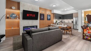 A modern living room with a grey sofa, a flat-screen TV, wooden cabinets, and a dining area with a table and chairs. - Boutique 3BR Townhouse • Free Parking • Sleeps 7 (Toronto)