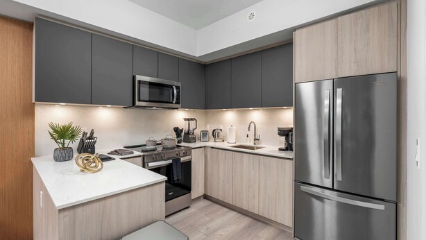 A modern kitchen with grey cabinets, a stainless steel refrigerator, a microwave, and a built-in oven. - Boutique 3BR Townhouse • Free Parking • Sleeps 7 (Toronto)