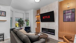 A modern living room with a sofa, a coffee table, a flat-screen TV, a fireplace, and a basketball jersey on the wall. - Boutique 3BR Townhouse • Free Parking • Sleeps 7 (Toronto)