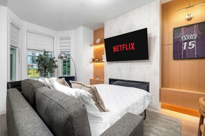Et moderne hotelværelse med en stor seng, en sofa, et fjernsyn ophængt på væggen og et vindue med persienner.