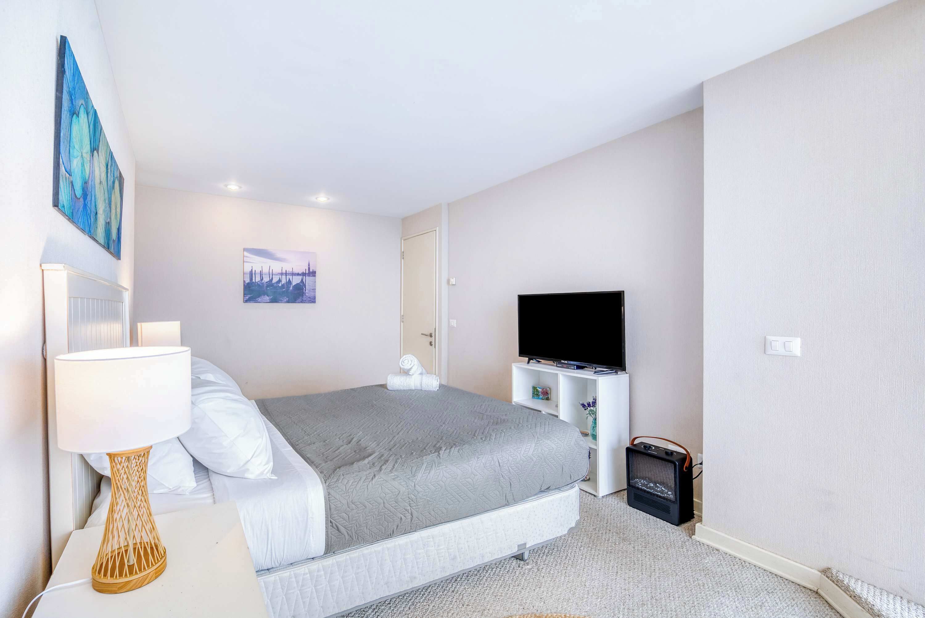 Une chambre à coucher avec un lit, une télévision, une lampe et un tableau au mur.