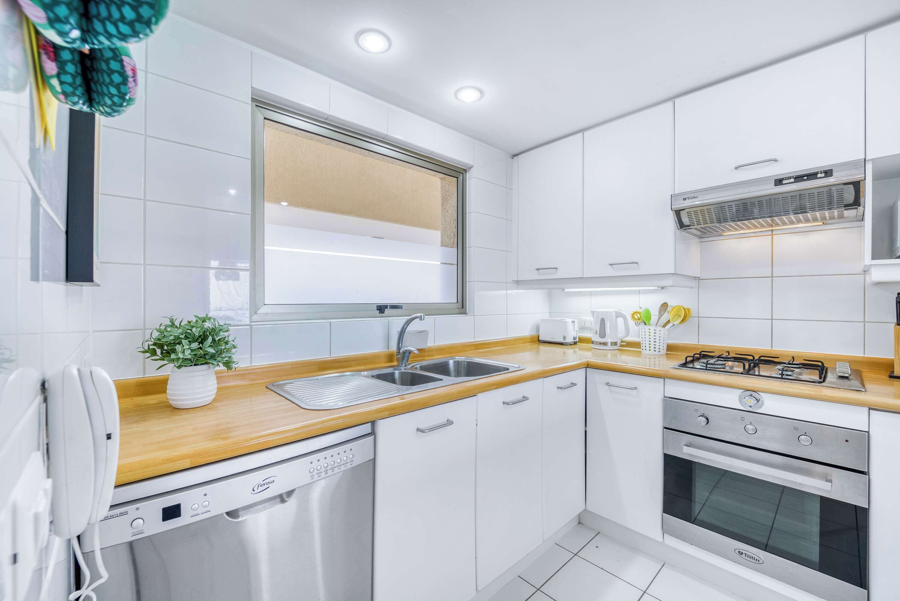Una cucina moderna con mobili bianchi, un piano di lavoro in legno, lavastoviglie integrata, un fornello e una finestra.