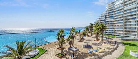 Um resort com praia, palmeiras e área de piscina.