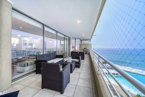 Un balcone con mobili in vimini, una parete vetrata e vista sull'oceano.