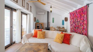 Un salon comprenant un canapé, des coussins, un ventilateur de plafond, un meuble en bois et une tapisserie colorée.
