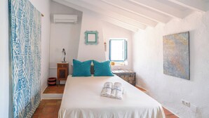 Une chambre à coucher avec un lit, des oreillers, une table de chevet, une fenêtre et un tableau au mur.
