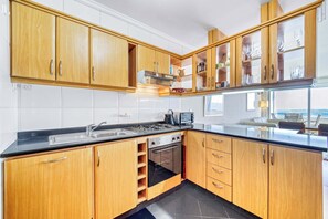 Eine Küche mit Holzausstattung, einer schwarzen Arbeitsplatte, Edelstahlgeräten und Blick aufs Meer.